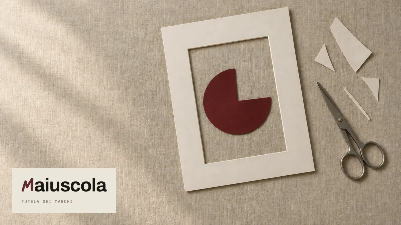 Un cerchio di carta rosso scuro con un quarto tolto, dentro una cornice di cartoncino chiaro, con forbici e ritagli accanto: copertina della guida su come registrare un logo